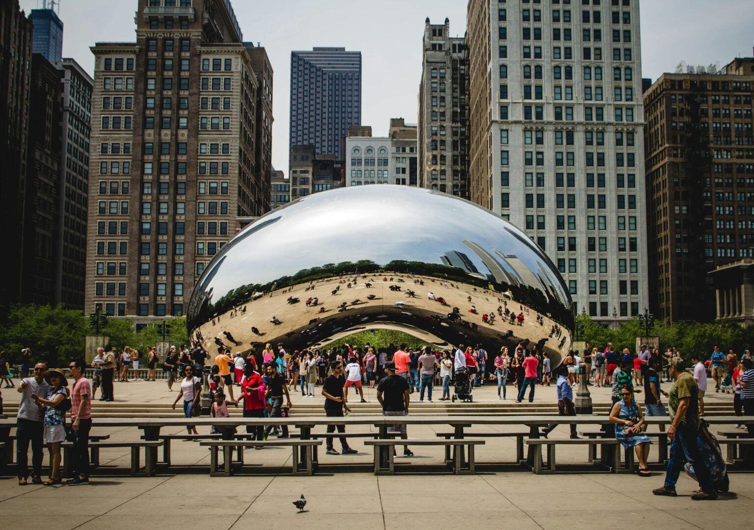 People gathering around Cloud Gate in Chicago with reflections of cityscapes. Popular tourist spot in Millennium Park.